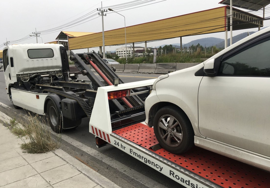 Professional tow truck operator loading a white sedan for emergency roadside assistance in Syracuse, Utah